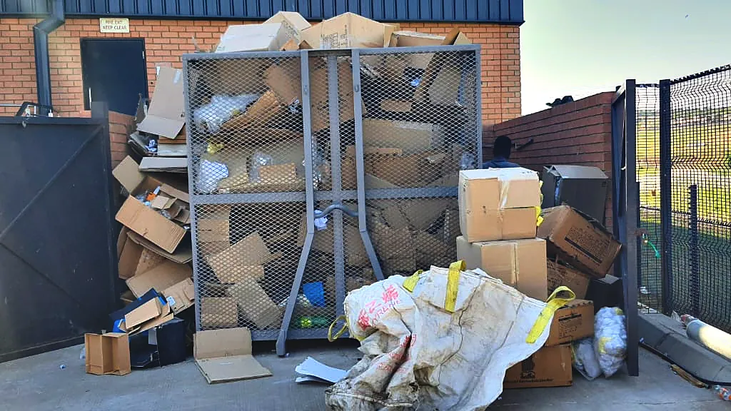A mesh cage at a warehouse service area with cardboard stacked beside it.